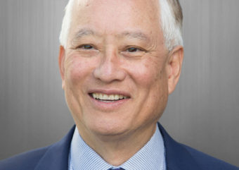 Dr. David Mee-Lee headshot smiling at camera wearing a navy suit, with blue tie and blue shirt